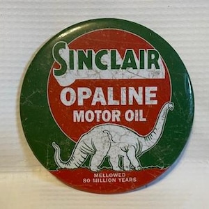 May include: A vintage Sinclair Opaline Motor Oil advertising button with a green and red background. The button features a white dinosaur with the text "Sinclair Opaline Motor Oil" and "Mellowed 80 Million Years".