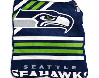 Puede incluir: Una manta azul marino y blanca de los Seattle Seahawks con el logotipo de la cabeza de águila del equipo y el nombre del equipo. La manta tiene rayas verdes y blancas y está hecha de un material suave.