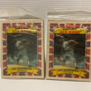 May include: Two vintage baseball cards featuring Dan Quisenberry of the Kansas City Royals. The cards are from the Kellogg's Corn Flakes All-Star series. The cards are in protective plastic sleeves.