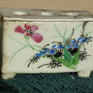 Könnte beinhalten: Ein weißer Porzellan-Tintenfass mit Deckel und Ausguss. Das Tintenfass ist mit einem floralen Design in Rosa, Blau, Grün und Schwarz verziert.