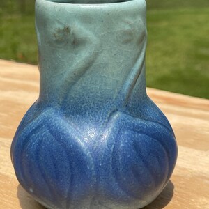 Op de afbeelding: Een kleine keramische vaas met een bolle basis en een cilindrische hals. De vaas heeft een tweekleurig blauw glazuur, dat overloopt van een lichter turquoise aan de bovenkant naar een diepblauw aan de basis. Het oppervlak heeft een getextureerd, gecraqueleerd uiterlijk.