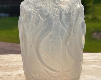 May include: A frosted glass perfume bottle with a cylindrical body and a rounded top. The bottle is adorned with a relief design of flowing, organic shapes. The bottle is translucent, allowing light to pass through, and has a matching stopper.