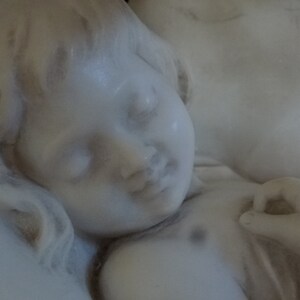 May include: A white marble sculpture of a sleeping child, with a soft, delicate face and flowing hair.