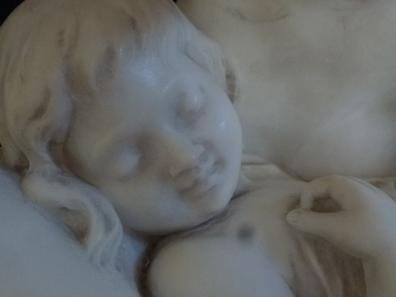 May include: A white marble sculpture of a sleeping child, with a soft, delicate face and flowing hair.