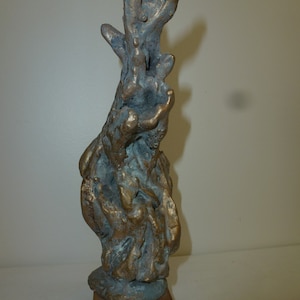 Puede incluir: Una escultura abstracta de bronce con una superficie rugosa y texturizada. La escultura está montada sobre una base de madera.