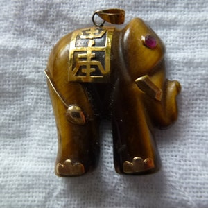 May include: A gold-toned tiger's eye elephant pendant with a red gemstone eye and Chinese characters on the back.
