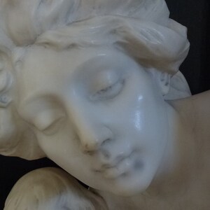 May include: A white marble sculpture of a woman's head and shoulders. The woman has her eyes closed and her head is tilted to the side. The sculpture is detailed and realistic.
