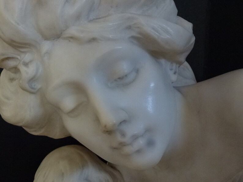 May include: A white marble sculpture of a woman's head and shoulders. The woman has her eyes closed and her head is tilted to the side. The sculpture is detailed and realistic.