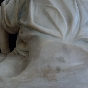 May include: A white marble sculpture of a seated figure with flowing drapery. The sculpture is signed "T.R." on the base.