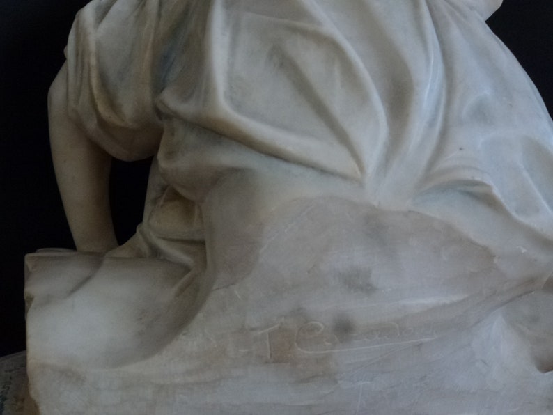 May include: A white marble sculpture of a seated figure with flowing drapery. The sculpture is signed "T.R." on the base.