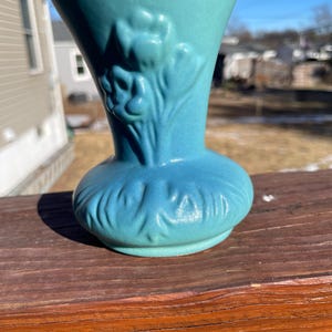 May include: A small, teal blue ceramic vase with a floral design. The vase has a wide mouth and a narrow base.
