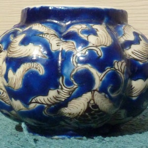 May include: A small, round, blue and white ceramic pot with a floral design. The pot has a glossy finish and is decorated with white flowers and leaves on a cobalt blue background.