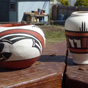 Può includere: Due piccoli vasi in terracotta dipinti a mano con motivi geometrici. Il vaso più grande è rotondo con un design rosso, bianco e nero. Il vaso più piccolo è più alto e ha un design bianco, arancione e nero.