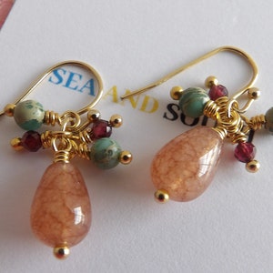 May include: Gold dangle earrings with a teardrop shaped peach colored stone and a cluster of smaller stones in shades of green and red.