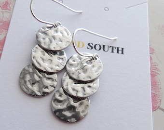 May include: Silver earrings with four hammered metal discs hanging from a silver hook. The earrings are displayed on a white card with the text "Sea and South" printed in black.
