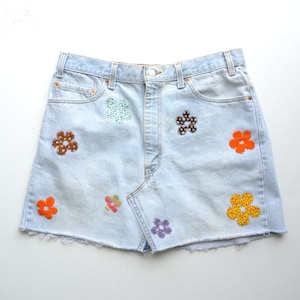 May include: A light blue denim skirt with a frayed hem and colorful flower appliques.