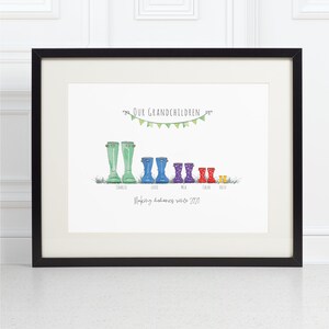 May include: A framed print featuring a watercolour illustration of colourful wellies lined up in a row. The text 'Our Grandchildren' is at the top with a bunting of flags. The text 'Making memories since 2020' is at the bottom. Each boot has a name underneath: Charlie, Lottie, Mia, Chloe, Ollie.