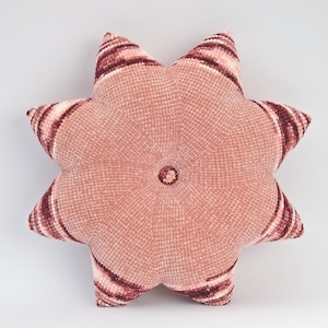 Może przedstawiać: Gwiaździsta poduszka w kolorze różowym i bordowym z fakturowaną powierzchnią.
