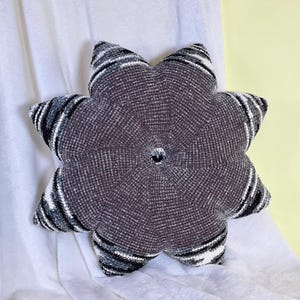 May include: A grey and white star-shaped cushion with a crocheted texture. The cushion has a black and white striped pattern around the edges.