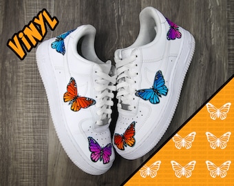 May include: White leather sneakers with butterfly designs. The butterflies are in various colors, including orange, blue, pink, and purple. The word "VINYL" is written in black letters on the top of the image.