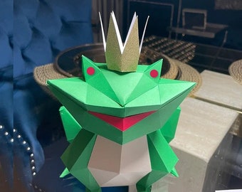 May include: A green origami frog wearing a gold and white crown. The frog has red eyes and a pink mouth.