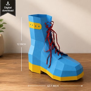 Puede incluir: Una bota de papel azul con suela y correa de tobillo amarillas, con cordones rojos. La bota tiene un diseño geométrico de bajo poligonaje. El texto indica una descarga digital y unas dimensiones de 30,48 cm de alto y 32,26 cm de largo.