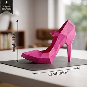 Op de afbeelding: Een felroze low-poly papieren schoen met hoge hak en een Mary Jane-bandje. Het object heeft een geometrisch gefacetteerd ontwerp en is gelabeld met afmetingen van 21 cm hoog en 28 cm diep. De afbeelding bevat een icoon voor digitale download.