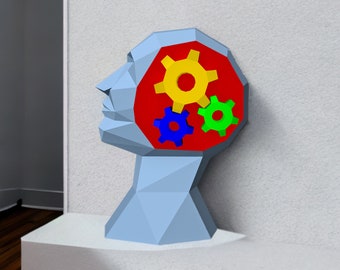 May include: A blue and gray geometric sculpture of a head with three colorful gears inside. The gears are yellow, blue, and green.
