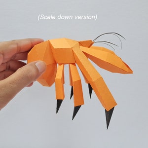 May include: An orange papercraft model of a crab with black claws and antennae. The crab is being held in someone's hand.