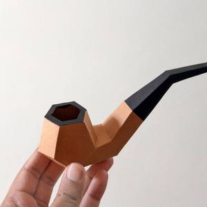 Peut inclure: Une pipe en papier brune et noire avec un bol hexagonal. La pipe est en papier et est un objet d&eacute;coratif.