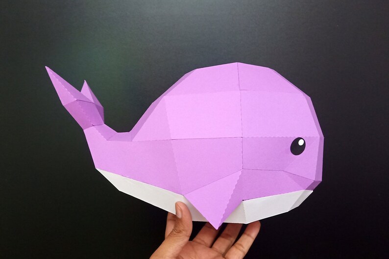 May include: A purple papercraft whale with a white belly. The whale is made of folded paper and has a 3D effect.