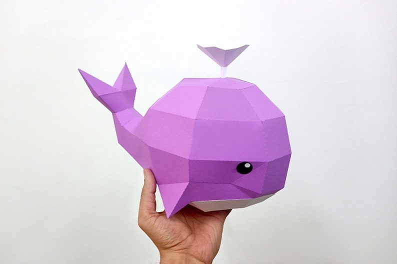 May include: A purple papercraft whale with a white fin on top. The whale has a white underside and black eyes.