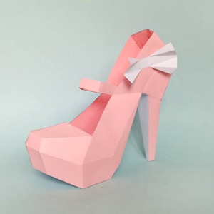 Puede incluir: Un zapato de tac&oacute;n alto de papel rosa con un lazo blanco. El zapato est&aacute; hecho de papel doblado y tiene un dise&ntilde;o geom&eacute;trico.