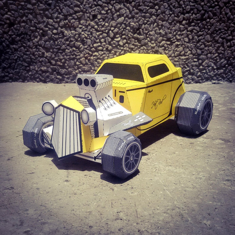 May include: A yellow paper model of a hot rod car with black tires and the words "Hot Rod" written on the side. The car has a large engine and a detailed interior.