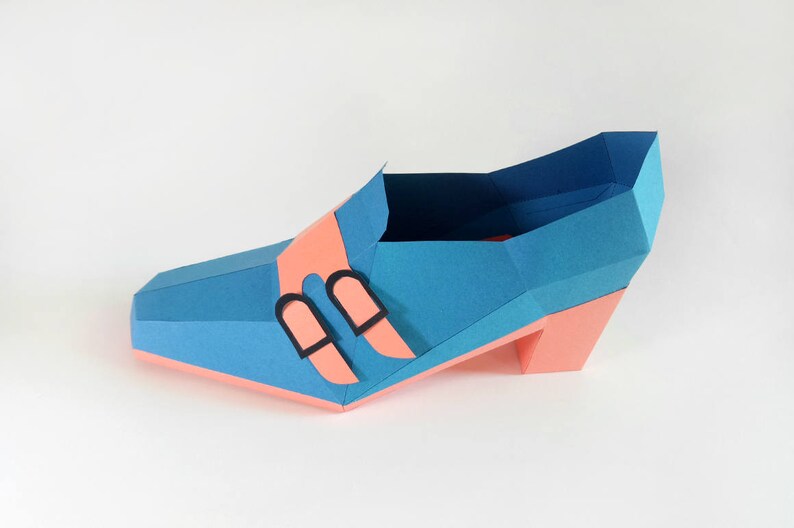 May include: A blue and pink papercraft shoe with black buckles. The shoe has a high heel and a pointed toe.