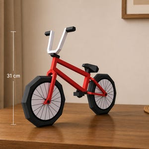 Puede incluir: Un modelo de bicicleta geométrica en rojo, blanco y negro con diseño low-poly, marco rojo, manillar blanco y neumáticos negros con radios blancos. La bicicleta mide 31 cm de altura, según lo indicado por una línea de medición vertical.