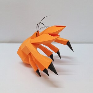 May include: An orange papercraft sculpture of a crab with black claws. The crab is made of folded paper and has a realistic appearance.