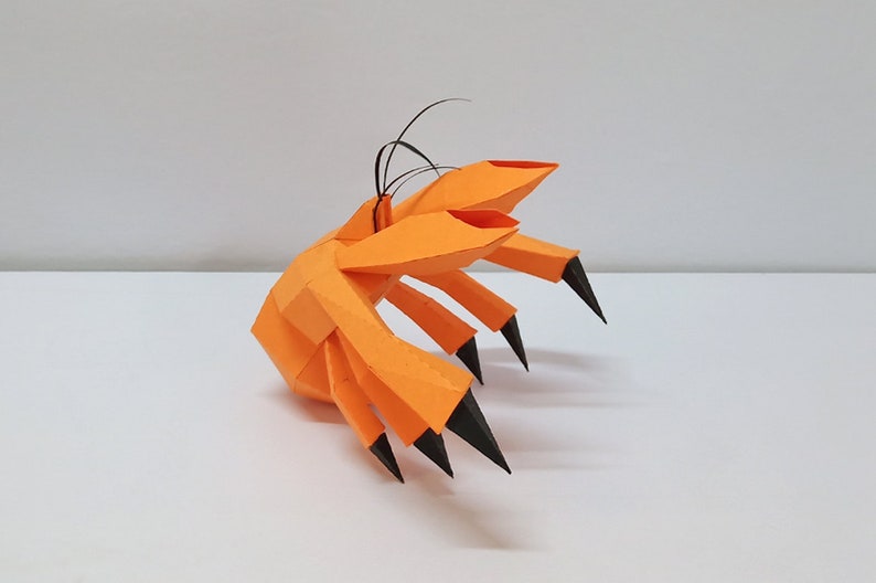 May include: An orange papercraft sculpture of a crab with black claws. The crab is made of folded paper and has a realistic appearance.