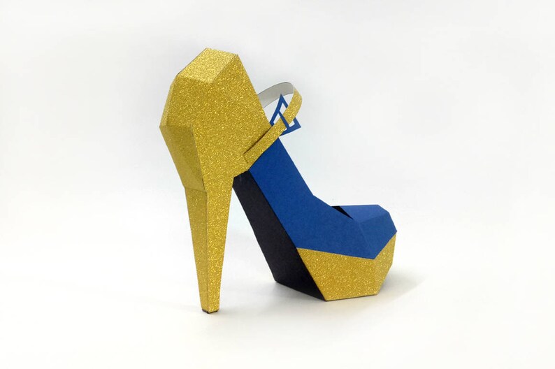 May include: A gold and blue papercraft high heel shoe. The shoe has a gold glitter finish and a blue strap.