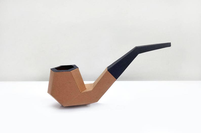 Peut inclure: Une pipe en carton brun avec un embout peint en noir. La pipe est faite de carton pli&eacute; et a une forme g&eacute;om&eacute;trique.