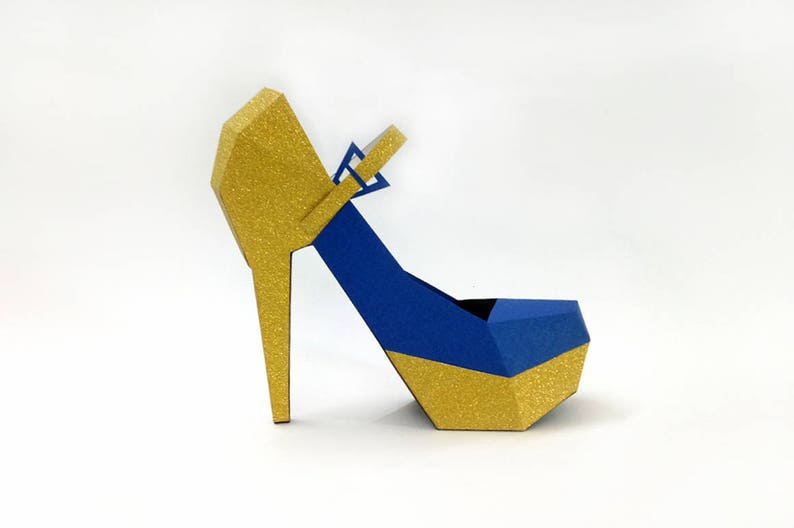 May include: A gold and blue high-heeled shoe with a geometric design. The shoe has a gold heel and a blue upper with a gold trim.