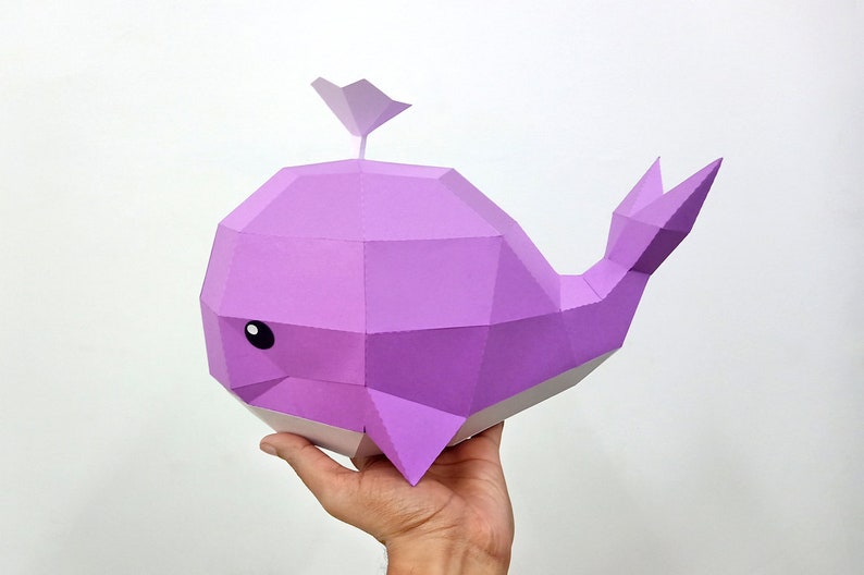 May include: A purple papercraft whale with a small fin on top. The whale has a white underside and black eyes.