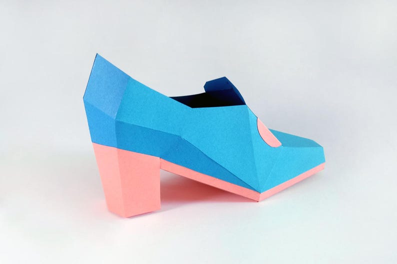 May include: A blue and pink origami shoe with a high heel. The shoe is made of paper and has a geometric design.