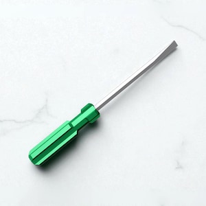 May include: A flathead screwdriver with a bright green handle and a silver blade. The tool is designed for turning screws with a single slot in their heads. The screwdriver is shown on a white marble surface.