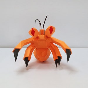May include: Orange and black papercraft model of a crab with red eyes. The crab has six legs and two antennae.