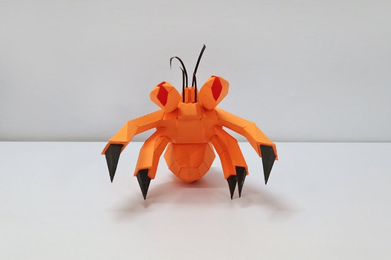 May include: Orange and black papercraft model of a crab with red eyes. The crab has six legs and two antennae.