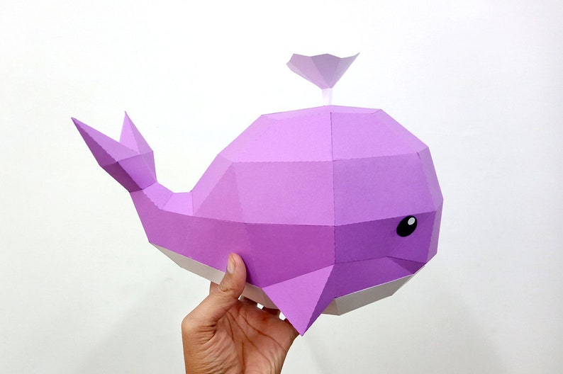 May include: A purple papercraft whale with a white underside and black eyes. The whale has a small fin on its back.