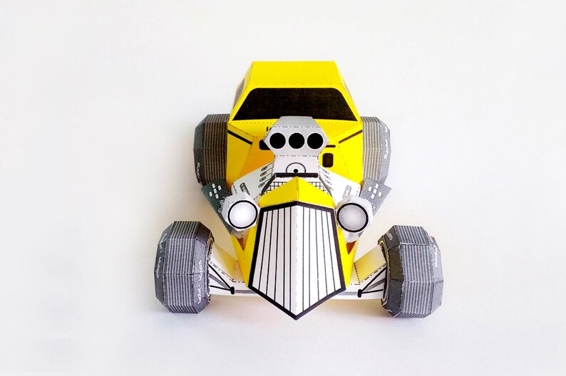 May include: A yellow papercraft model of a hot rod car with black and white details. The car has a large engine with three exhaust pipes and large black tires.