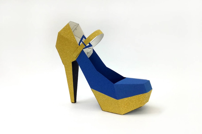 May include: A blue and gold high-heeled shoe with a gold glitter finish. The shoe has a strap across the top of the foot.
