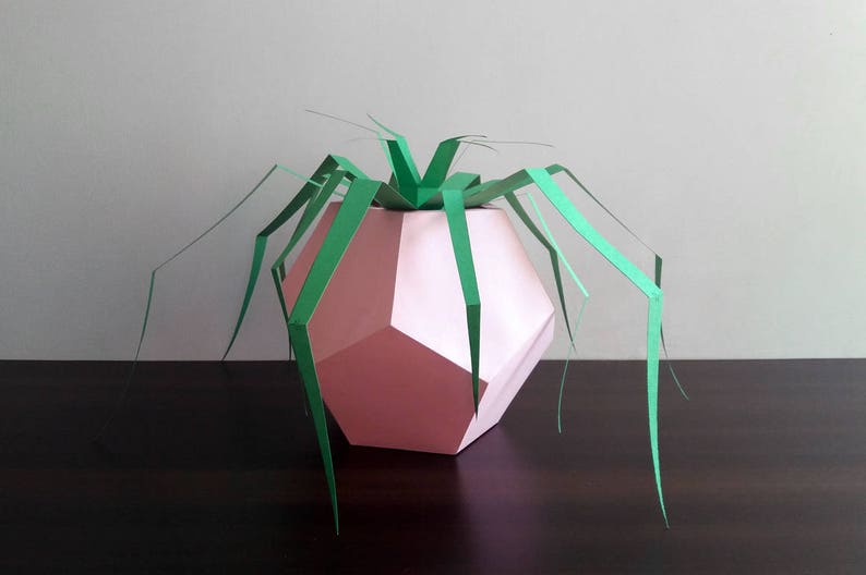 May include: A pink geometric paper vase with green paper leaves. The vase is made of folded paper and has a unique, modern design.
